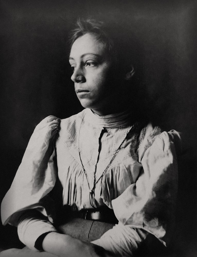 A photograph of Käthe Kollwitz, née Schmidt, aged around 23, sitting against a dark background. She is looking to the left and wearing a white blouse. Photographer unknown. This vintage photograph from the estate of Mathilde Rüstow, a donation by Alexandra Aichberger, is held in the archives of Kollwitz Museum Köln, Inv. No. F-01.a-03.