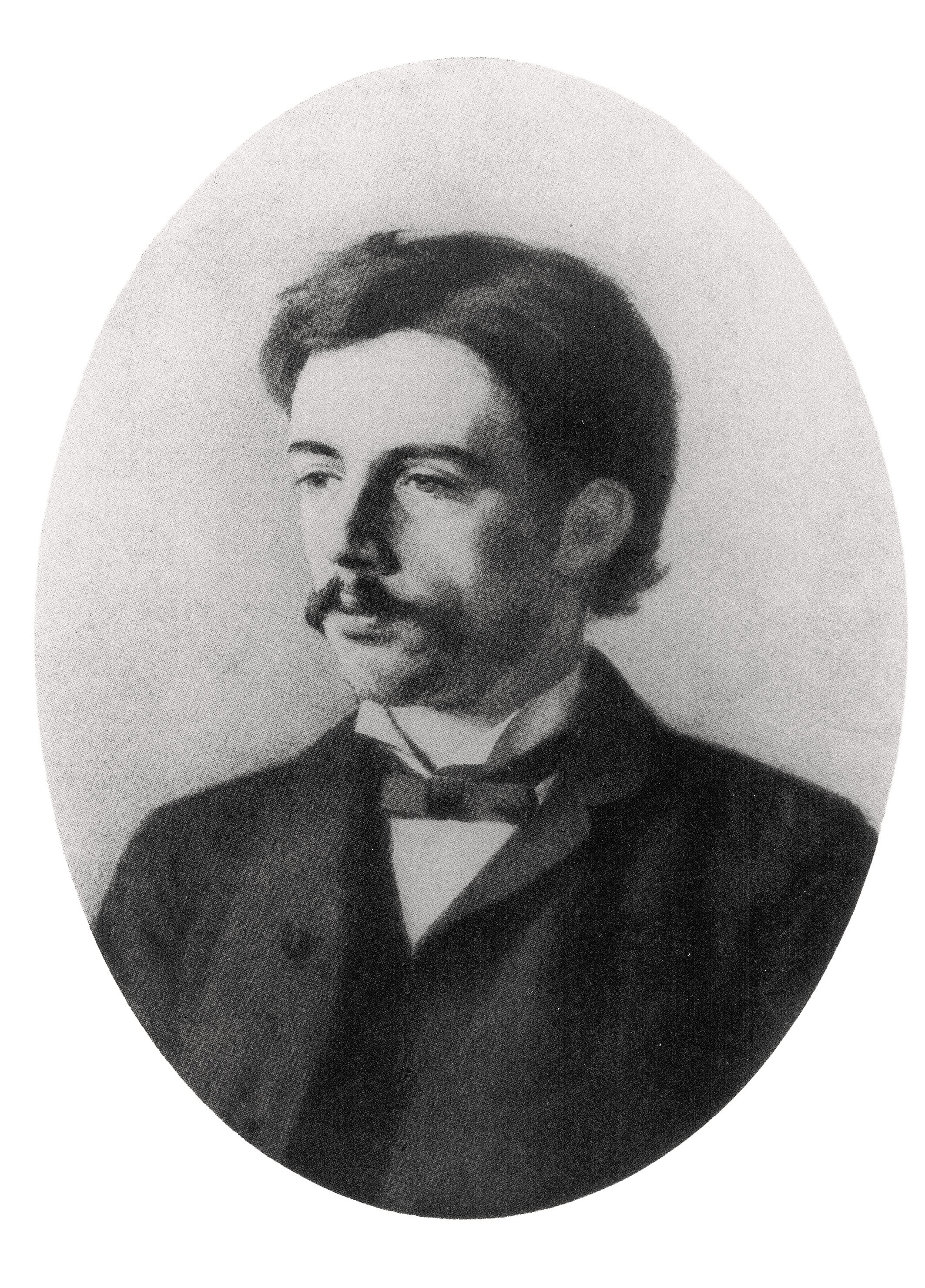 This black-and-white portrait, a photograph of a lost painting by Käthe Kollwitz dating from around 1886/87, shows a three-quarter-length bust portrait of her brother Konrad Schmidt as a young man with dark hair and a distinctive moustache, presented within an oval frame. He gazes slightly to the left and wears contemporary formal attire consisting of a dark jacket, a light-coloured waistcoat, and a dark bow tie. The background is plain and light in tone.
