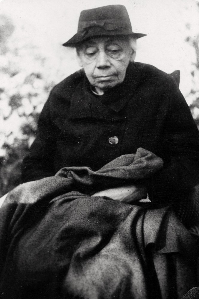 Dieses Schwarz-Weiß-Porträt aus den Jahren um 1944/45 zeigt die betagte Käthe Kollwitz in einer sitzenden, in sich gekehrten Haltung, wobei ihr Oberkörper das Bildzentrum füllt. Sie trägt einen dunklen, schlichten Hut und einen schweren Mantel, während ihr gefurchtes Gesicht mit fast geschlossenen Augen eine tiefe, meditative Ruhe ausstrahlt. Ihre Hände ruhen unsichtbar unter einer schweren dunklen Decke auf ihrem Schoß. Es ist die vielleicht letzte Aufnahme der Künstlerin, entstanden in Moritzburg. Fotograf ist Hartmut Reiche. Ein Reproabzug aus dem Nachlass der Künstlerin befindet sich im Archiv des Kollwitz Museum Köln, Inv. Nr. F-01.a-49. 