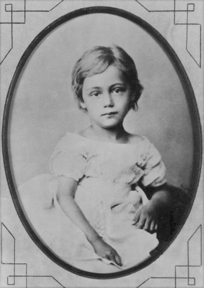 Eine Fotografie von Käthe Kollwitz, geborene Schmidt, im Alter von etwa 5 Jahren. Sie trägt ein weißes Klein mit kurzen Ärmeln. Fotograf:in unbekannt. Ein Repro-Abzug des Bildes aus dem Nachlass der Künstlerin befindet sich im Archiv des Kollwitz Museum Köln, Inv. Nr. F-01.a-01.