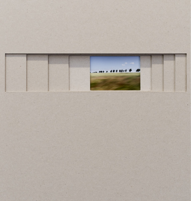 Dieses Kunstwerk besteht aus einer großen, minimalistischen Fläche aus graubraunem Karton, in deren oberem Drittel ein schmaler, horizontaler Schlitz eingeschnitten ist. Durch diese schieberartige Aussparung blickt man auf ein kleines, eingebettetes Farbfoto, das eine Landschaft im Vorbeifahren zeigt. Während der Himmel blau und eine Baumreihe am Horizont scharf zu erkennen sind, ist die grüne Wiese im Vordergrund durch die Bewegungsunschärfe der Reise stark verwischt.