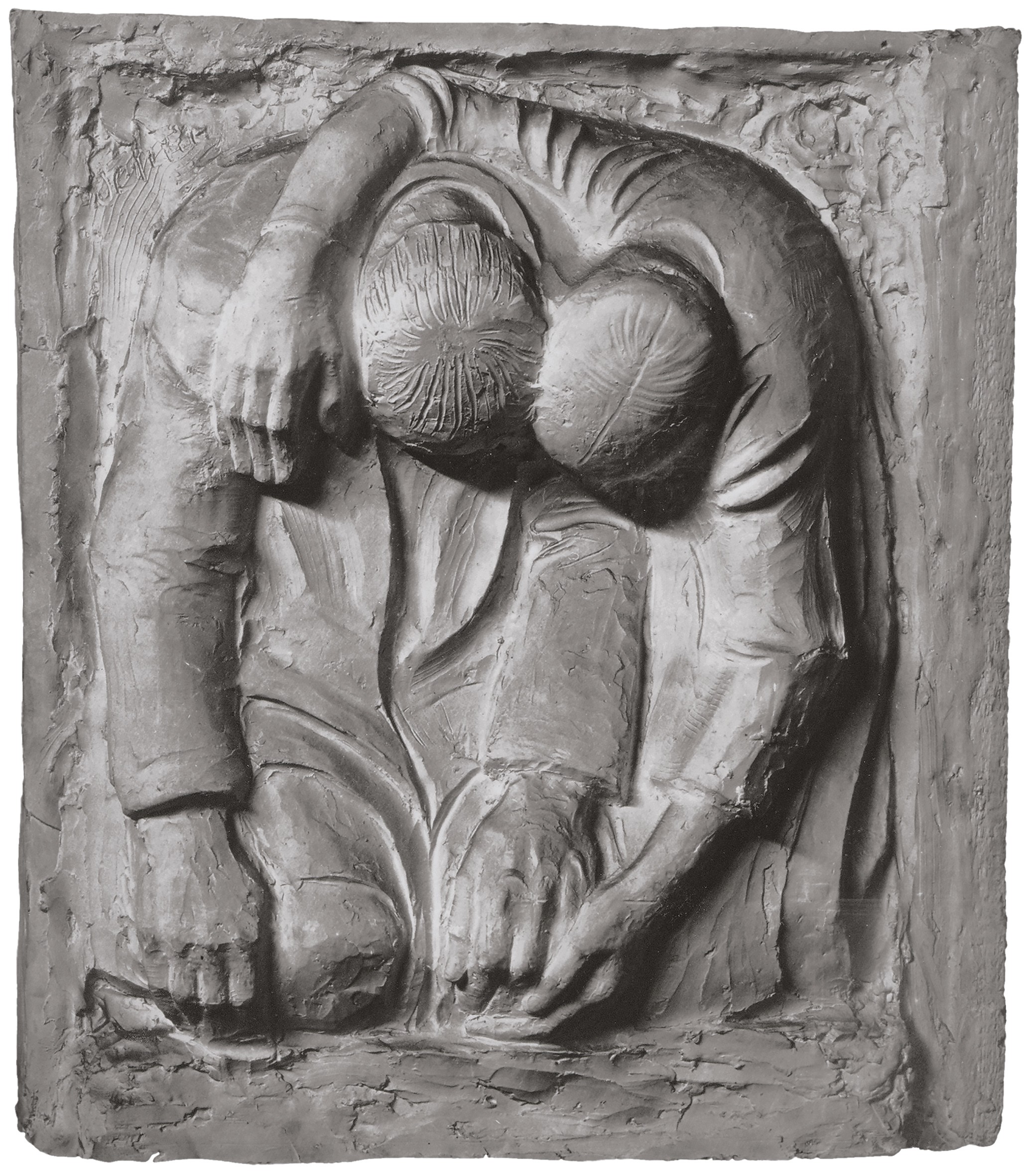 The black-and-white image shows a plaster relief depicting two figures bent deeply forward, clinging tightly to one another in profound grief. One arm rests protectively over the other’s shoulder, while their heads droop listlessly forward and touch. The rough, block-like texture of the surfaces reinforces the impression of deep sorrow and mutual support.